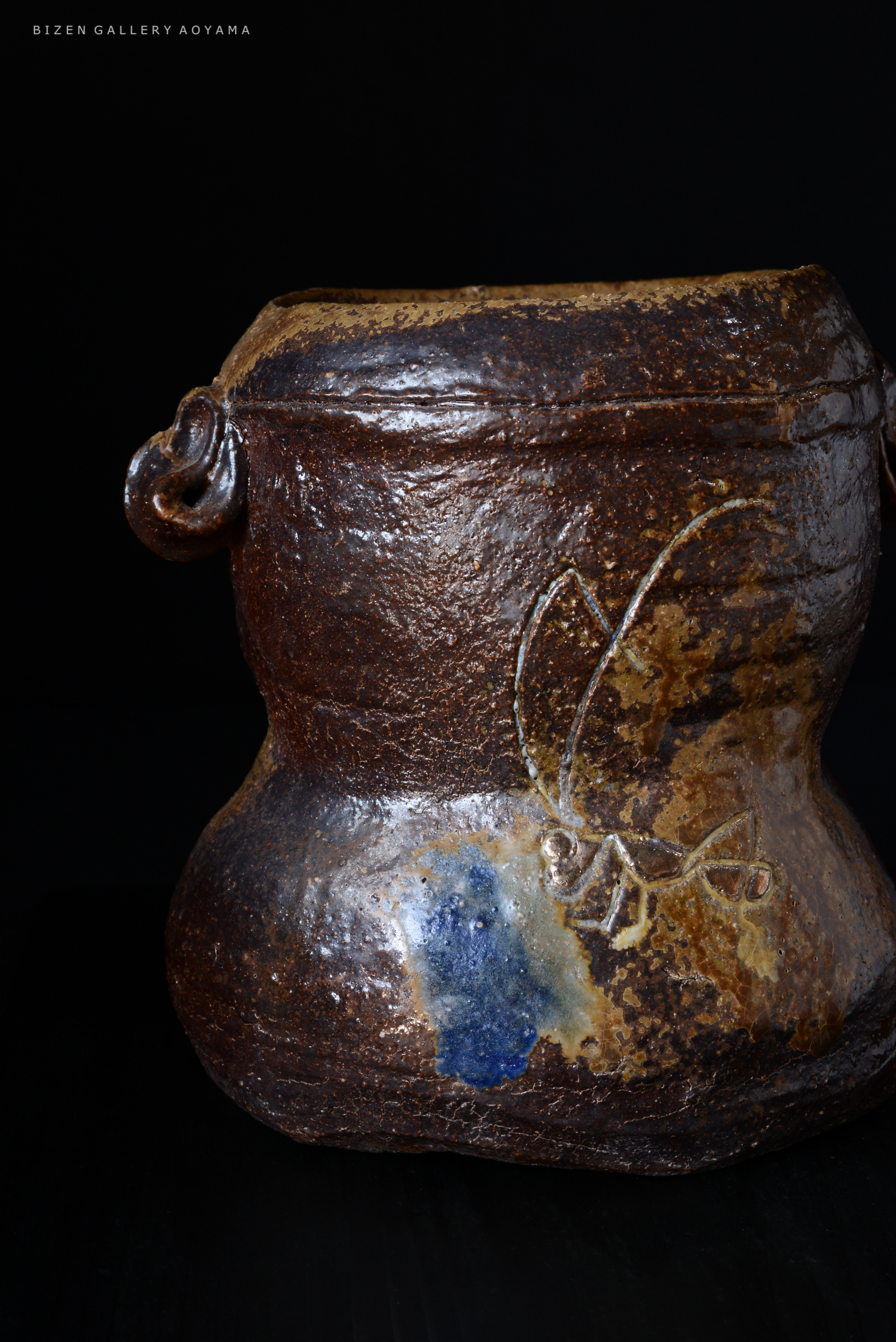 Close-up of a traditional Bizen pottery jar featuring a decorative design and glazes in earthy tones against a dark background.