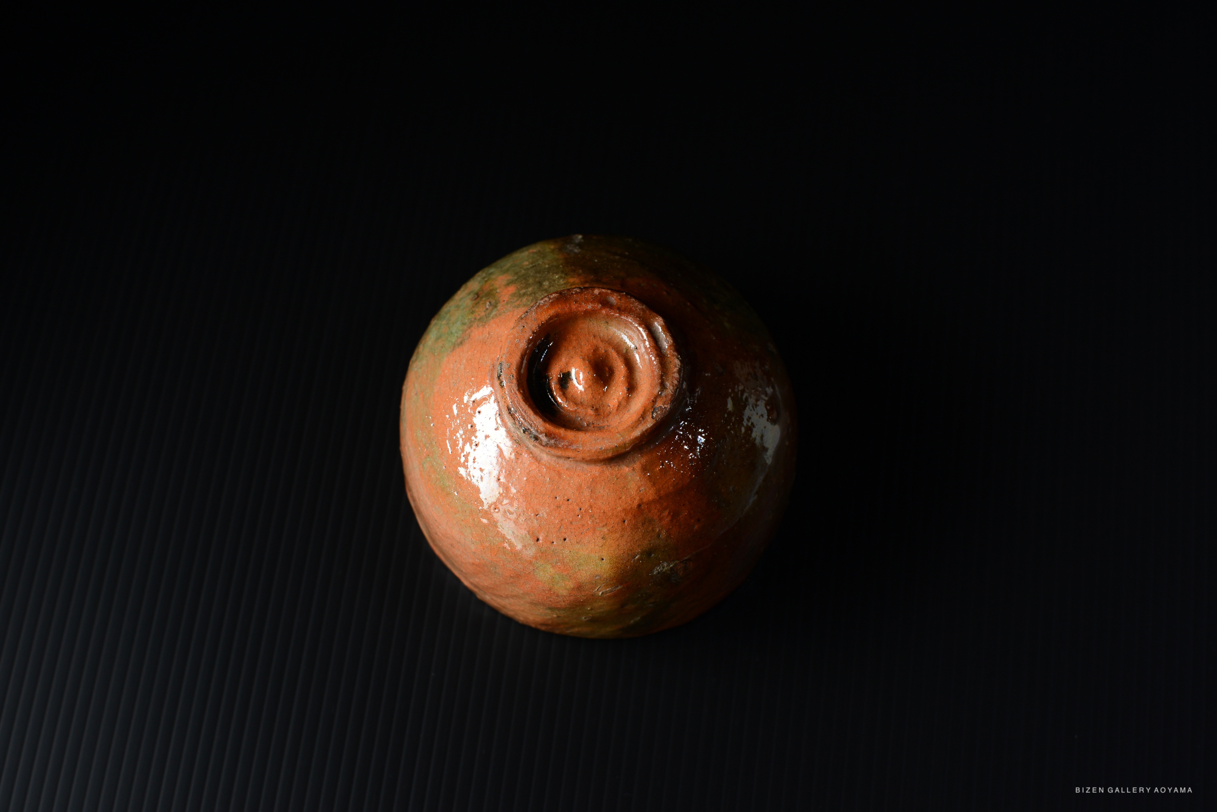A top view of a rustic, handcrafted ceramic pot with an earthy orange glaze, displaying a spiral design at the base.