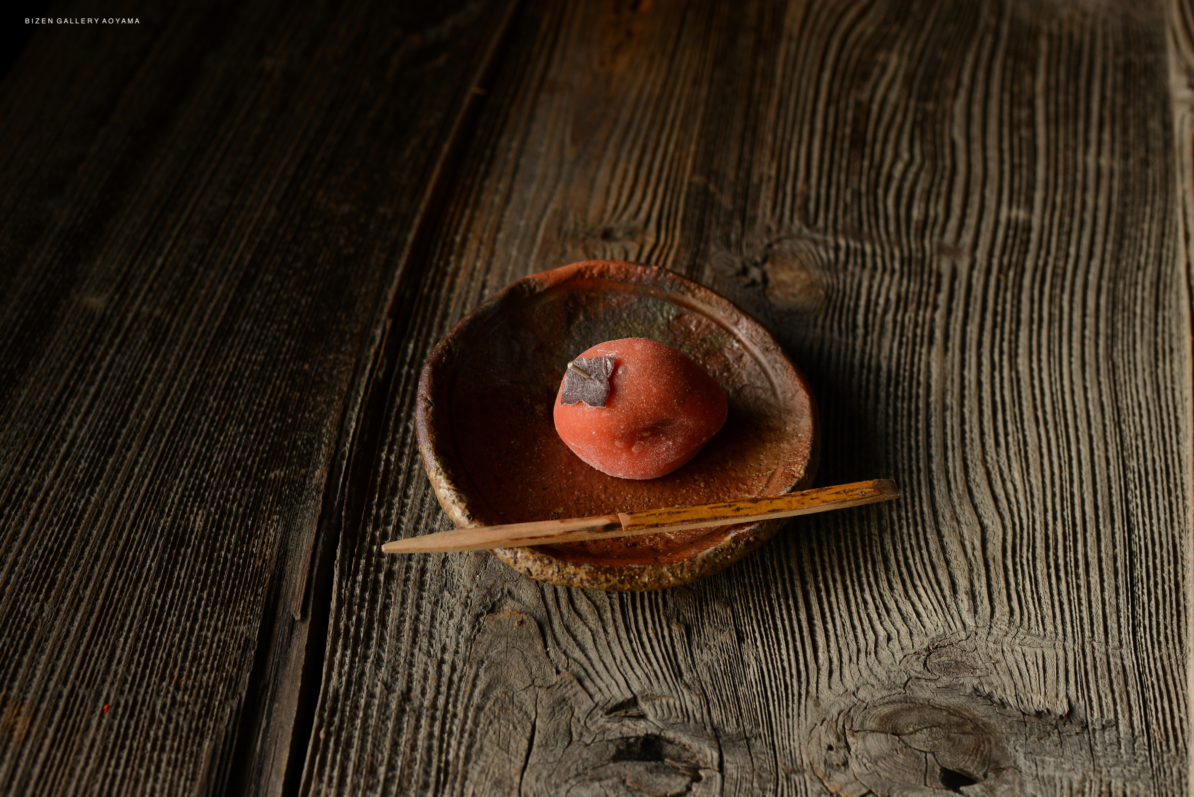 A smooth red dessert placed on a rustic brown plate, accompanied by a wooden chopstick, on a wooden table.